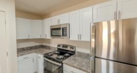 Renovated kitchen featuring white shaker cabinets, stainless steel appliances including refrigerator, oven, and microwave, plus granite-style countertops with ample workspace.