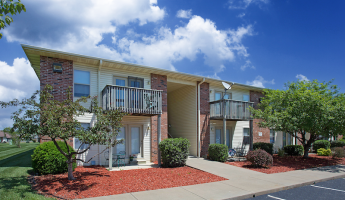 Two-story apartment building with brick and siding exterior, private balconies and patios, and landscaped grounds with trimmed shrubs, trees, and mulch beds